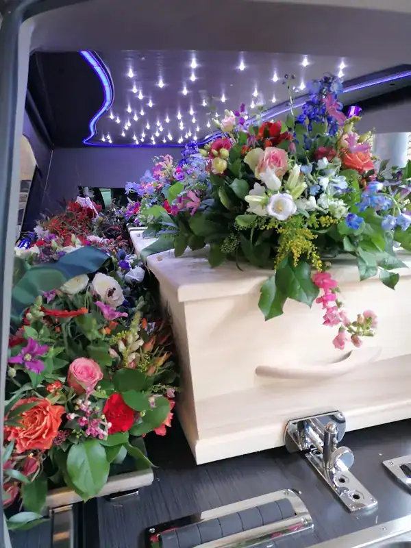 Een mooi versierde uitvaartkist met bloemen, geplaatst in een rouwwagen, symboliseert liefde en afscheid. Passend voor een respectvolle uitvaart verzorgd door De Dageraad Uitvaartverzorging.