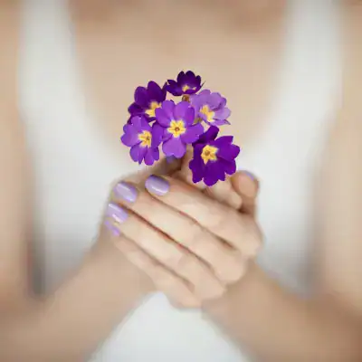 Vrouw houdt paarse bloemen vast, symbool voor herinnering en rouwverwerking bij uitvaartzorg, zachte kleuren en respectvolle sfeer.