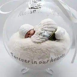 Een vredige baby in een heldere glazen grafdoos met tekst "Forever in our hearts", symboliseert liefde en herinnering voor overledenen in uitvaartverzorging.