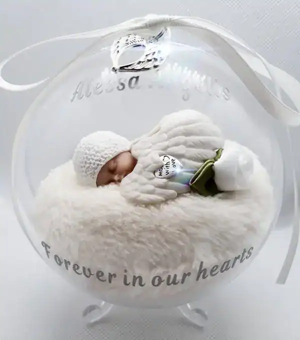Een vredige baby in een heldere glazen grafdoos met tekst "Forever in our hearts", symboliseert liefde en herinnering voor overledenen in uitvaartverzorging.