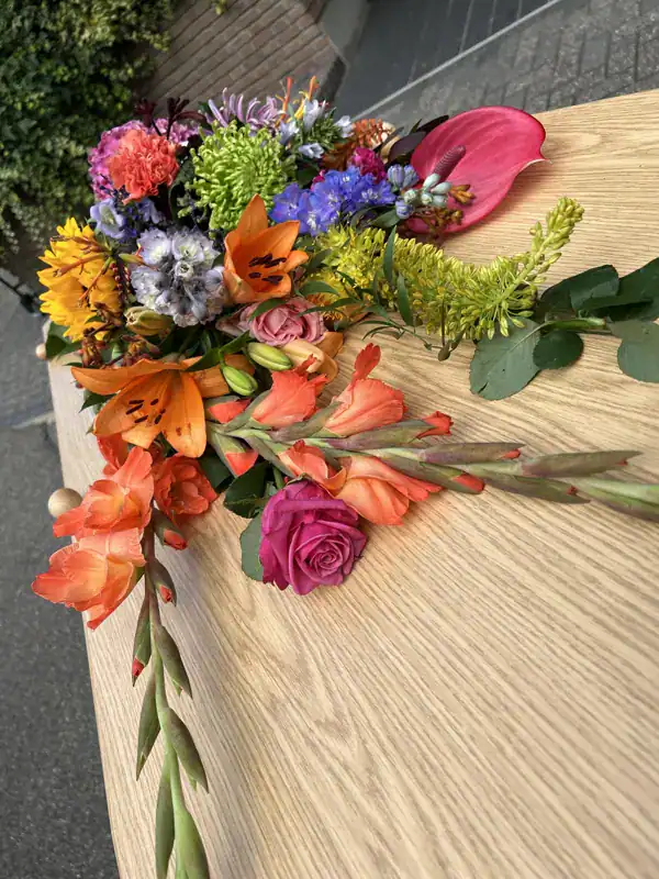 Lijkschik bloemenkrans voor uitvaartbedekking met kleurrijke bloemen en groene bladeren, symboliseert respect en herinnering voor afscheid. Vakkundige uitvaartverzorging door De Dageraad Uitvaartverzorging.