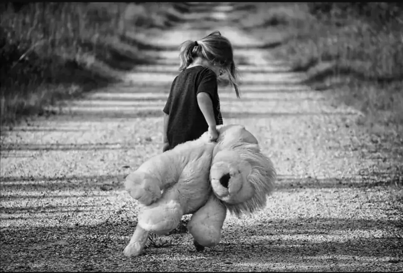 Onzeker meisje met knuffel op weg op een landweggetje, zwart-wit foto.