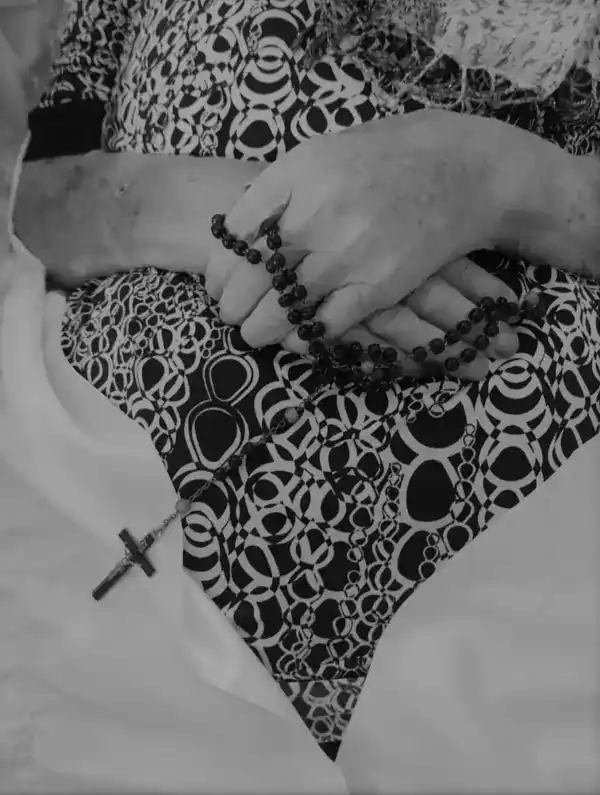 Rouw, hand met rozenkrans en kruis, symboliek van verdriet en kracht, zwart-wit foto, respectvolle uitvaartuitvaartzorg, ingetogen en sereen moment voor afscheid.