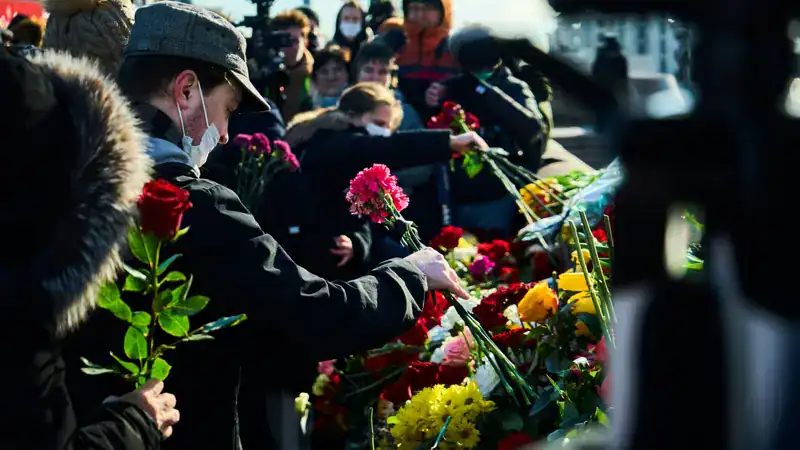Vrouw legt bloemen neer tijdens uitvaart ceremonie met veel publiek, symbool van respect en herinnering.